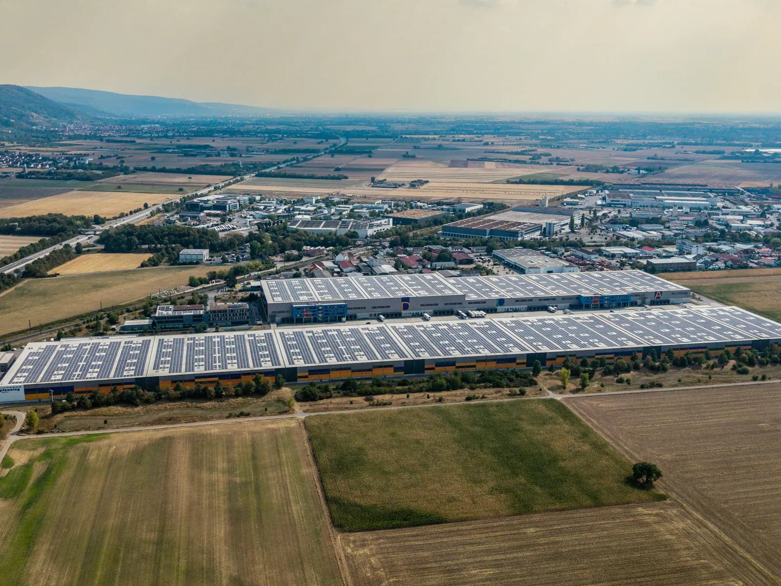 Industriehalle mit grossflächiger Solaranlage auf dem Dach, dahinter das Gewerbequartier und Felder