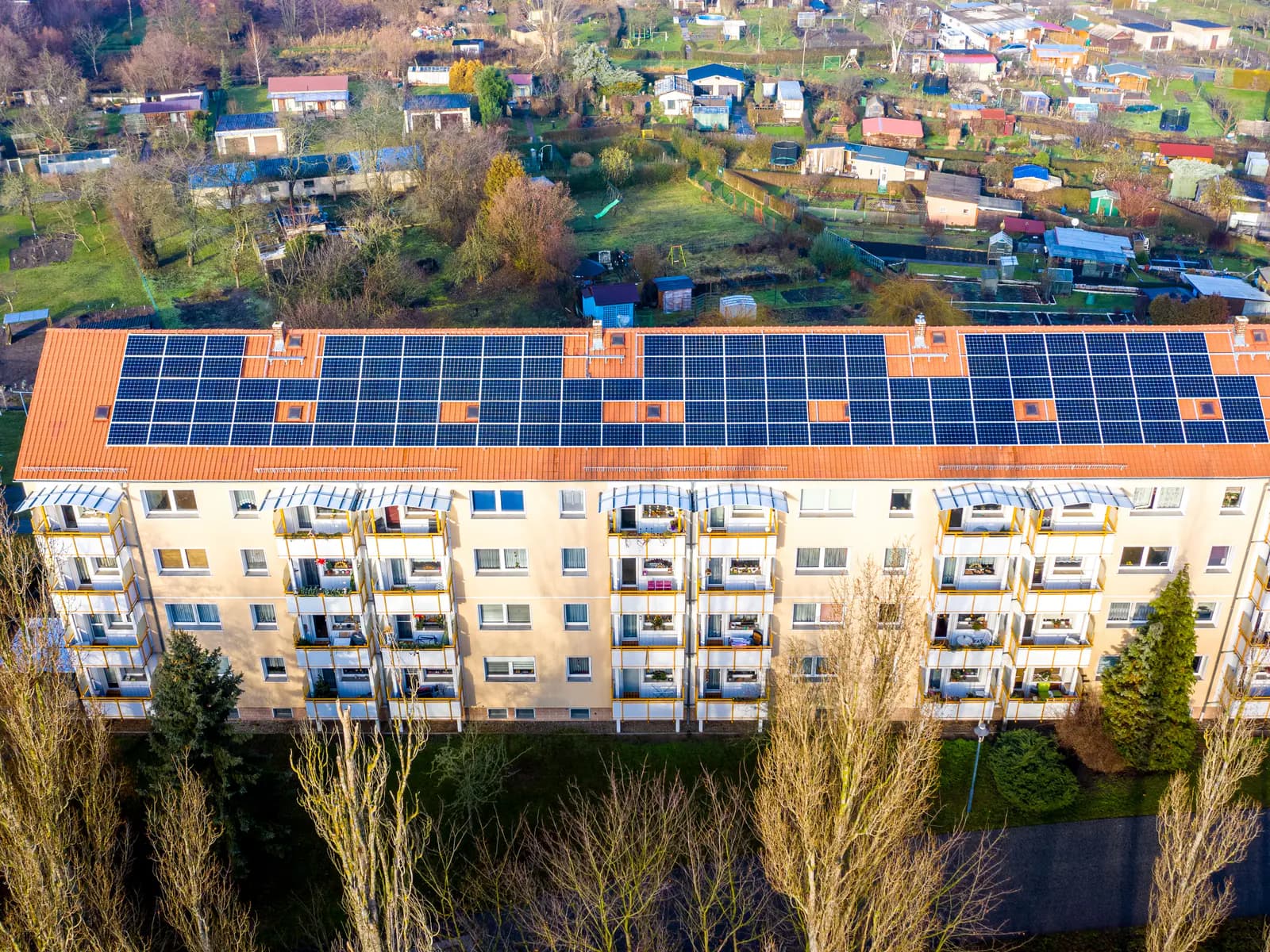 Mehrfamilienhaus, dessen Satteldach vollflächig mit Solarmodulen belegt ist, aufgenommen aus der Luft